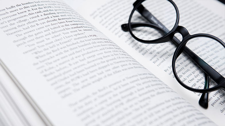 영어책이 펼쳐져 있고, 검은색 뿔테 안경이 책 위에 있다.