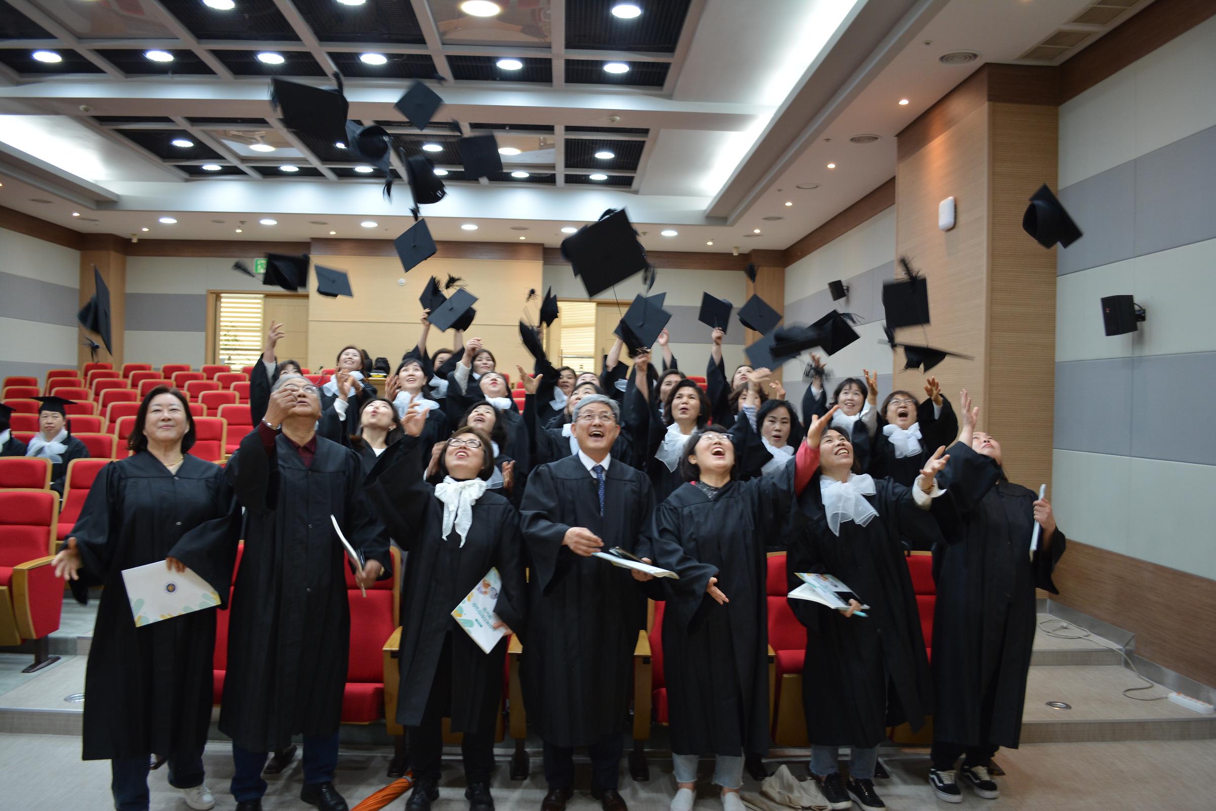 콘서트홀에서 학생들과 교수님이 웃으면서 학사모를 던지고 있는 사진