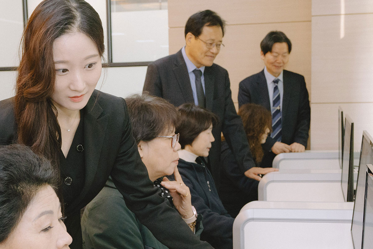 교수가 컴퓨터를 보며 학생 한명 한명 에게 지도를 하고 있다.