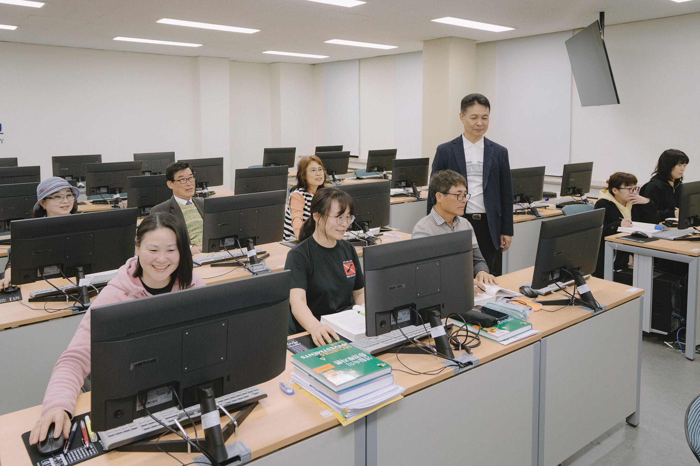 컴퓨터 실에서 수업을 듣는 학생들의 사진. 각자 모니터 앞에 앉아 집중하고 있다.