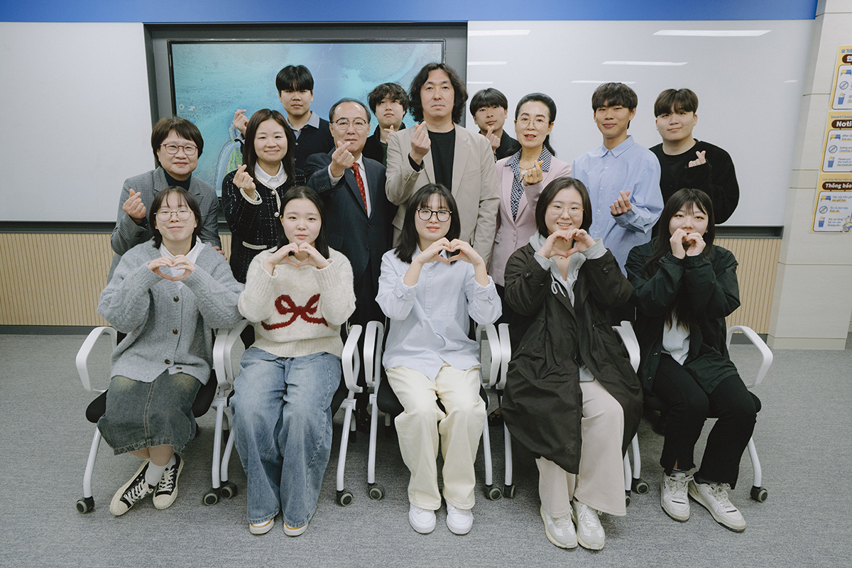 손가락 하트를 하며 의자에 앉은 학생들과 그 뒤에 서있는 학생들과 교수님들 사진