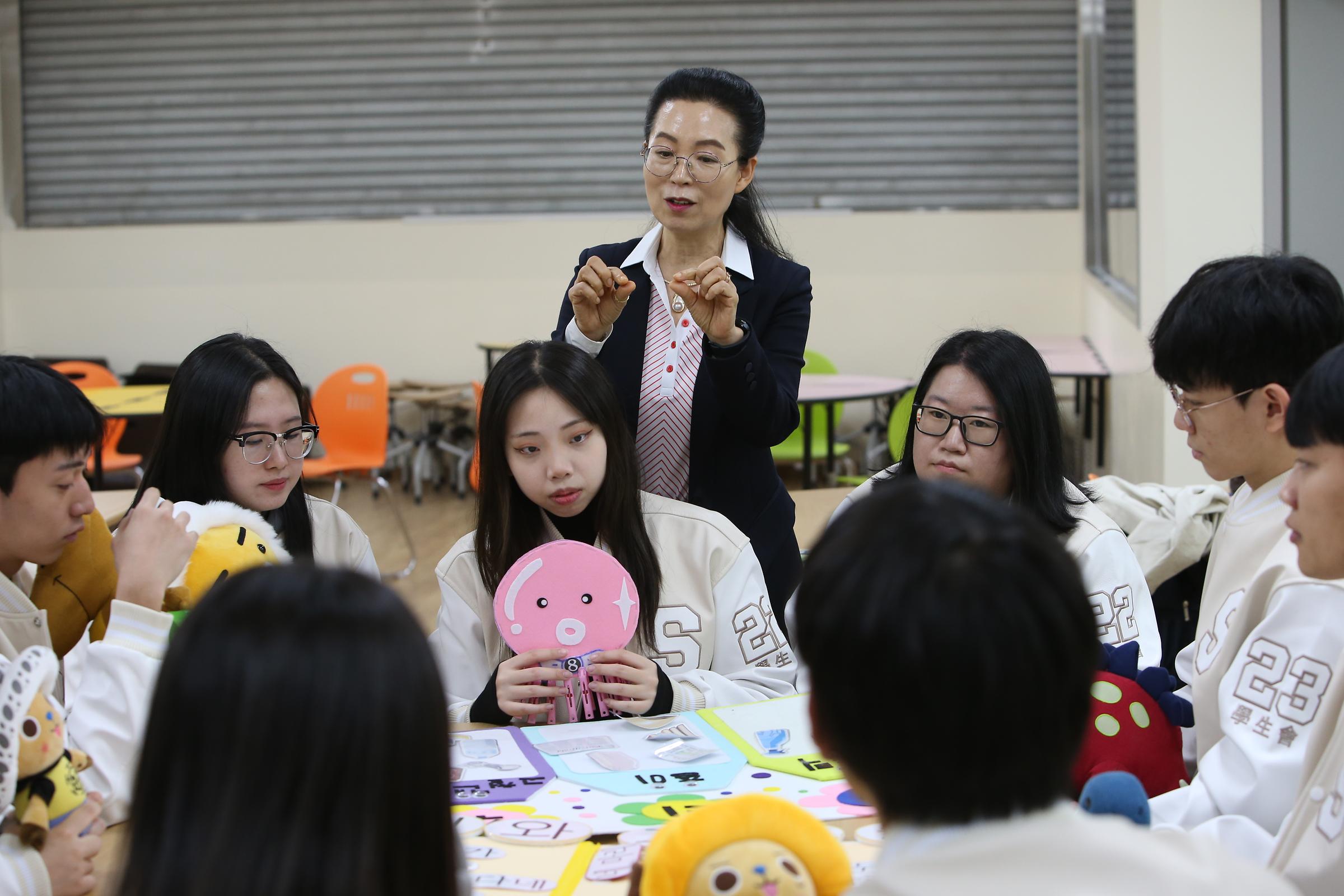 아동용 교재를 두고 둘러 앉은 학생들과 강의하는 교수님 사진