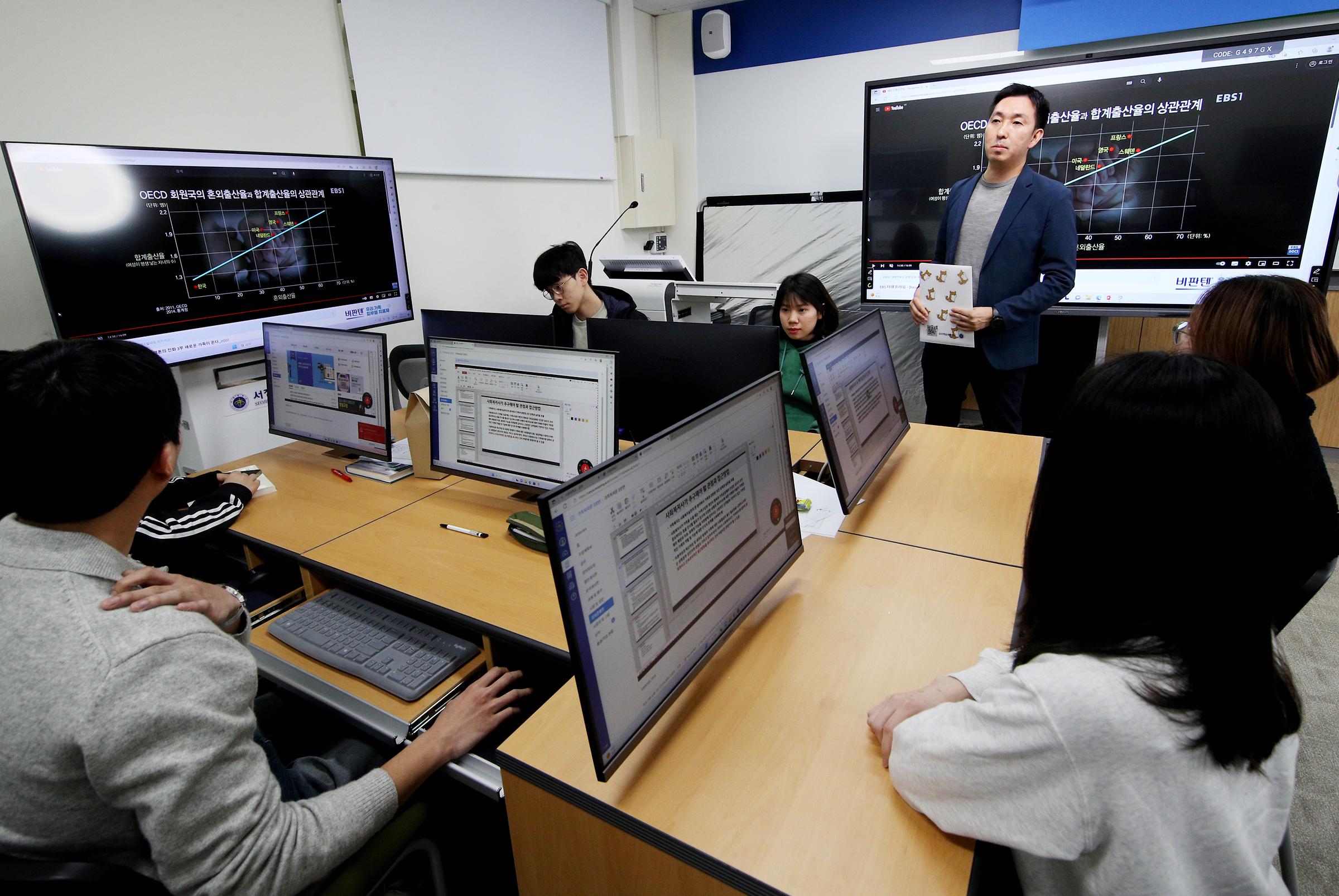 컴퓨터실에서 화면에 그래프를 키고 수업하는 교수님과 학생들