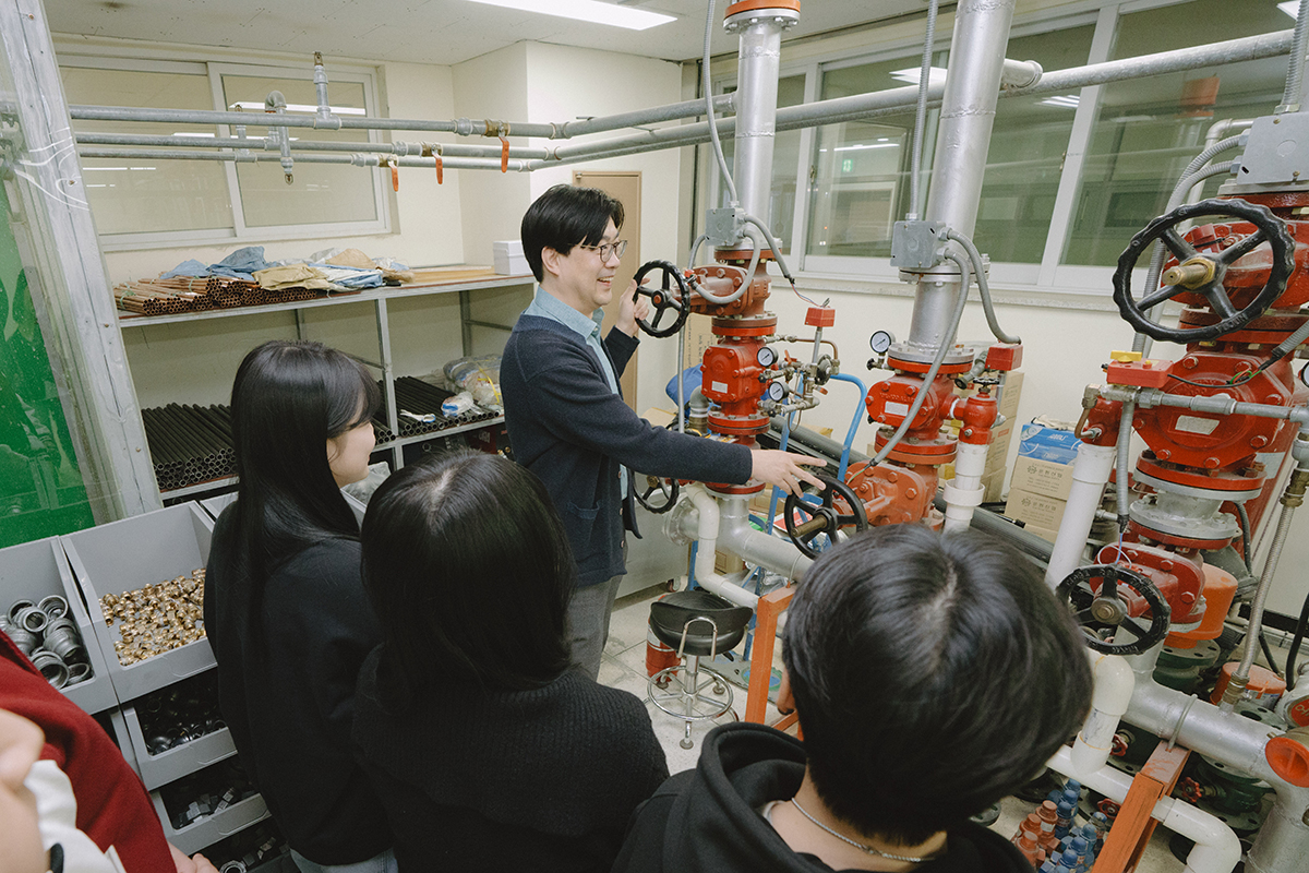 소방관련 기계 앞에서 시범을 보이는 교수님과 집중하여 보고있는 학생들 사진